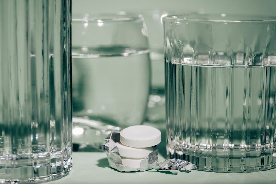 Vita tabletter i folie framför flera glas med klar vätska