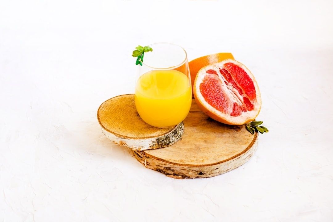 Glas med gul juice bredvid en halverad grapefrukt på träfat