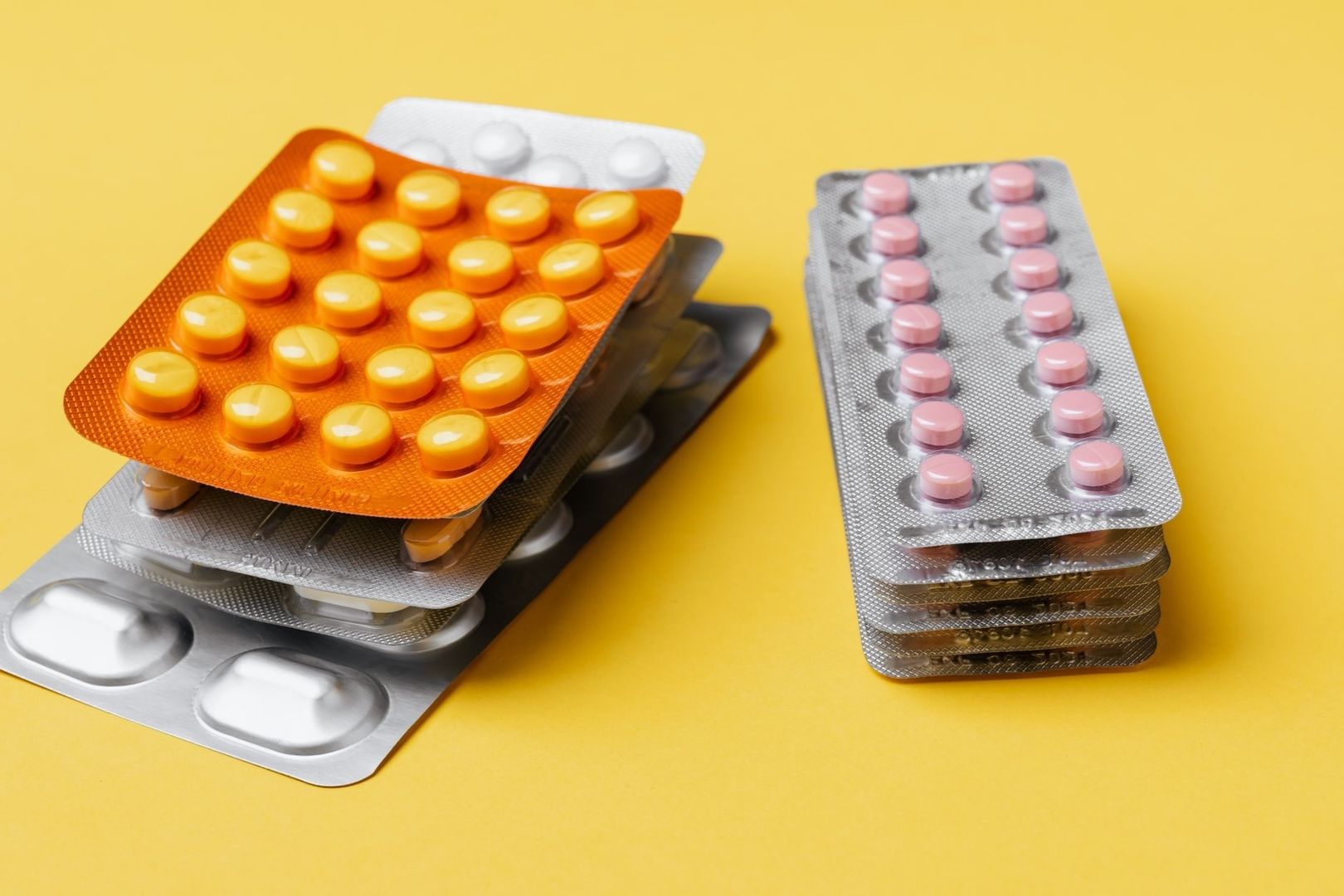 Blisterförpackningar med orange, rosa och vita tabletter på gul bakgrund